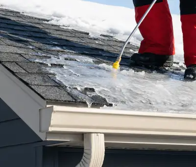 Ice dam removal technician using a steam wand to melt thick ice buildup on a residential roof in Cambridge, MA