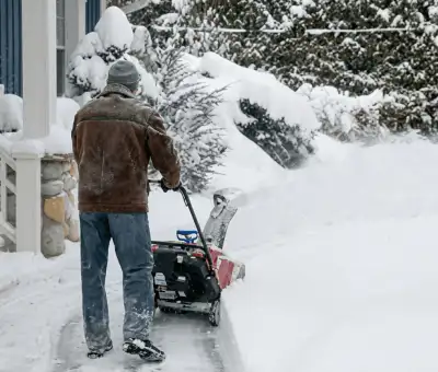 Residential snow removal technician using a snow blower to clear a home driveway and walkway in Cambridge, MA