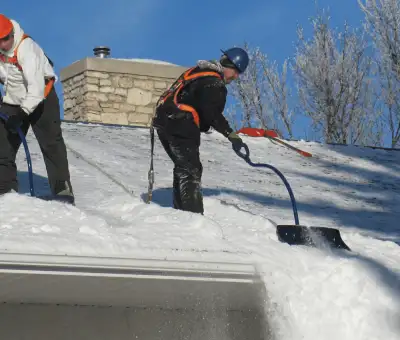 Professional technicians performing roof snow removal with safety harnesses and shovels in Cambridge, MA